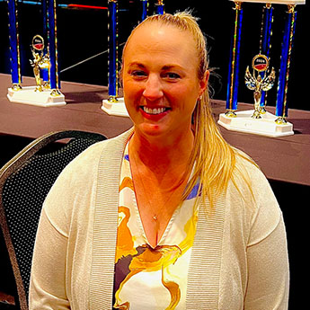 Lauren Gates smiling at the camera with blue and gold trophies in the background