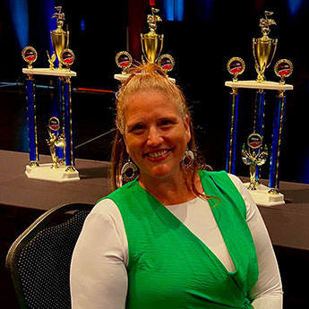 Sandie Kersten in a green top smiling at the camera with gold and blue statues in the background